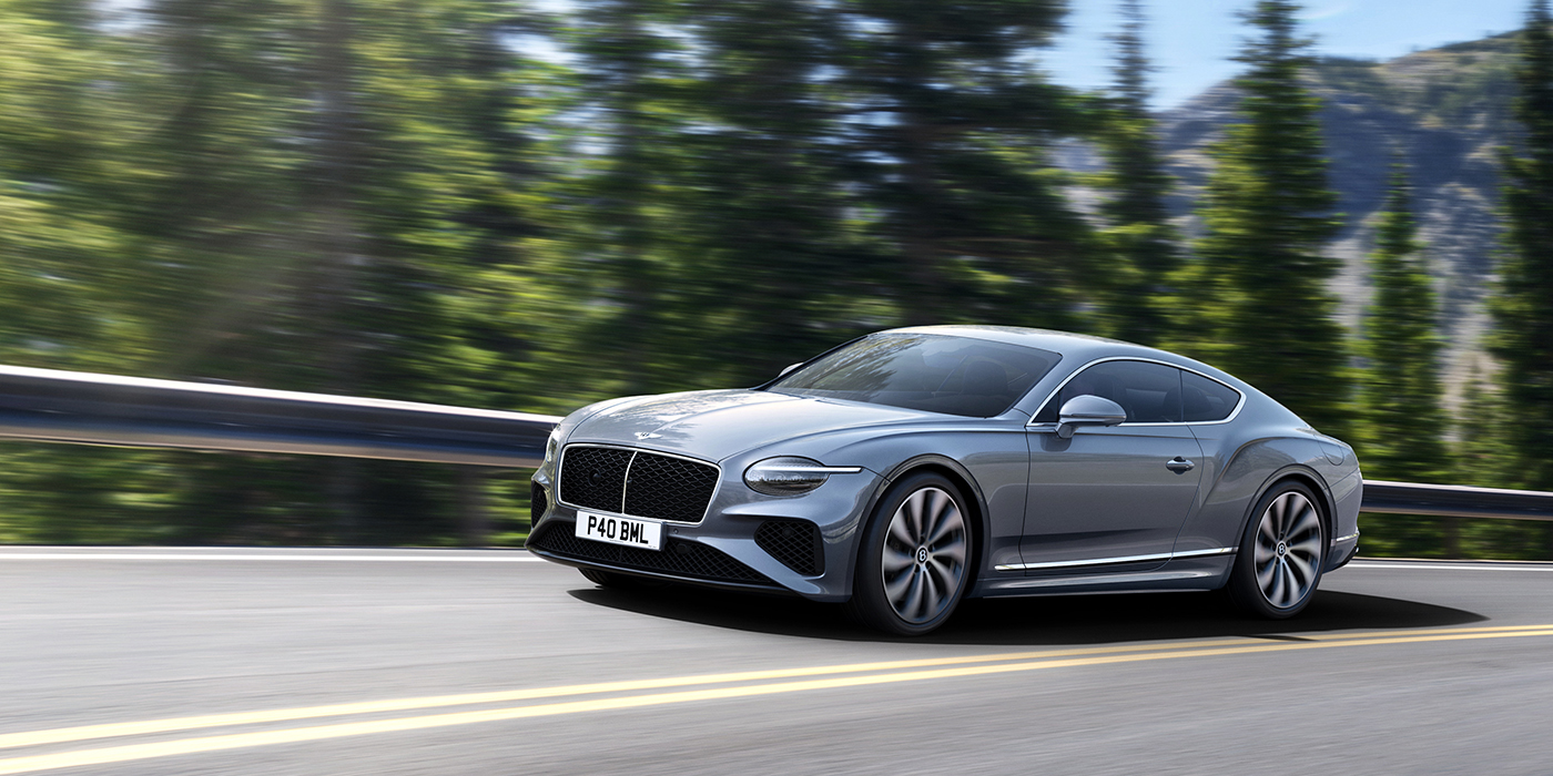 Bentley Kuala Lumpur New Bentley Continental GT coupe in Silverlake paint and 22 inch ten-spoke wheels, driving dynamically on a tree-lined road in the sunshine