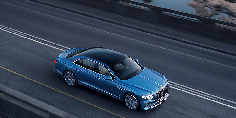 Bentley Kuala Lumpur New Bentley Flying Spur Azure sedan in Light windsor blue paint by Mulliner, with 22 inch Azure wheels seen from overhead driving dynamically on a country road