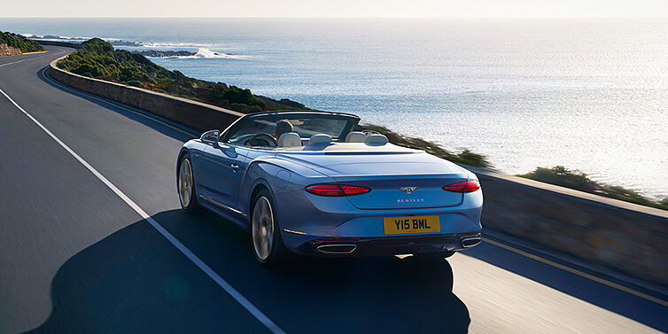 Bentley Kuala Lumpur New Bentley Continental GTC Azure convertible rear view in Light Windsor blue paint with 22 inch ten spoke wheels driving dynamically on an ocean road in the sunshine