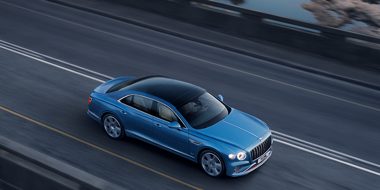 Bentley Kuala Lumpur New Bentley Flying Spur Azure sedan in Light windsor blue paint by Mulliner, with 22 inch Azure wheels seen from overhead driving dynamically on a country road