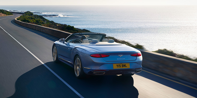 Bentley Kuala Lumpur New Bentley Continental GTC Azure convertible rear view in Light Windsor blue paint with 22 inch ten spoke wheels driving dynamically on an ocean road in the sunshine