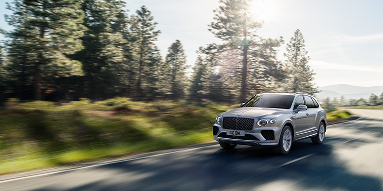 Bentley Kuala Lumpur Bentley Bentayga SUV front three quarter in Moonbeam silver paint driving dynamically along a tree-lined road