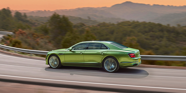 Bentley Kuala Lumpur Bentley Flying Spur Speed sedan side profile in Tourmaline Green paint driving dynamically on a mountain road at sunset